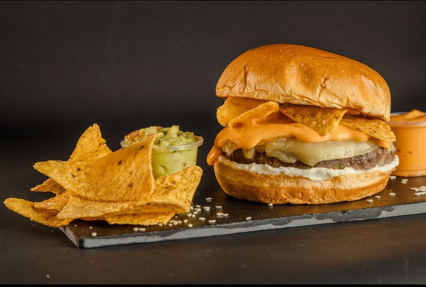 Beef burger served with brioche bun, cheddar cheese, special mayonnaise, guacamole and nachos